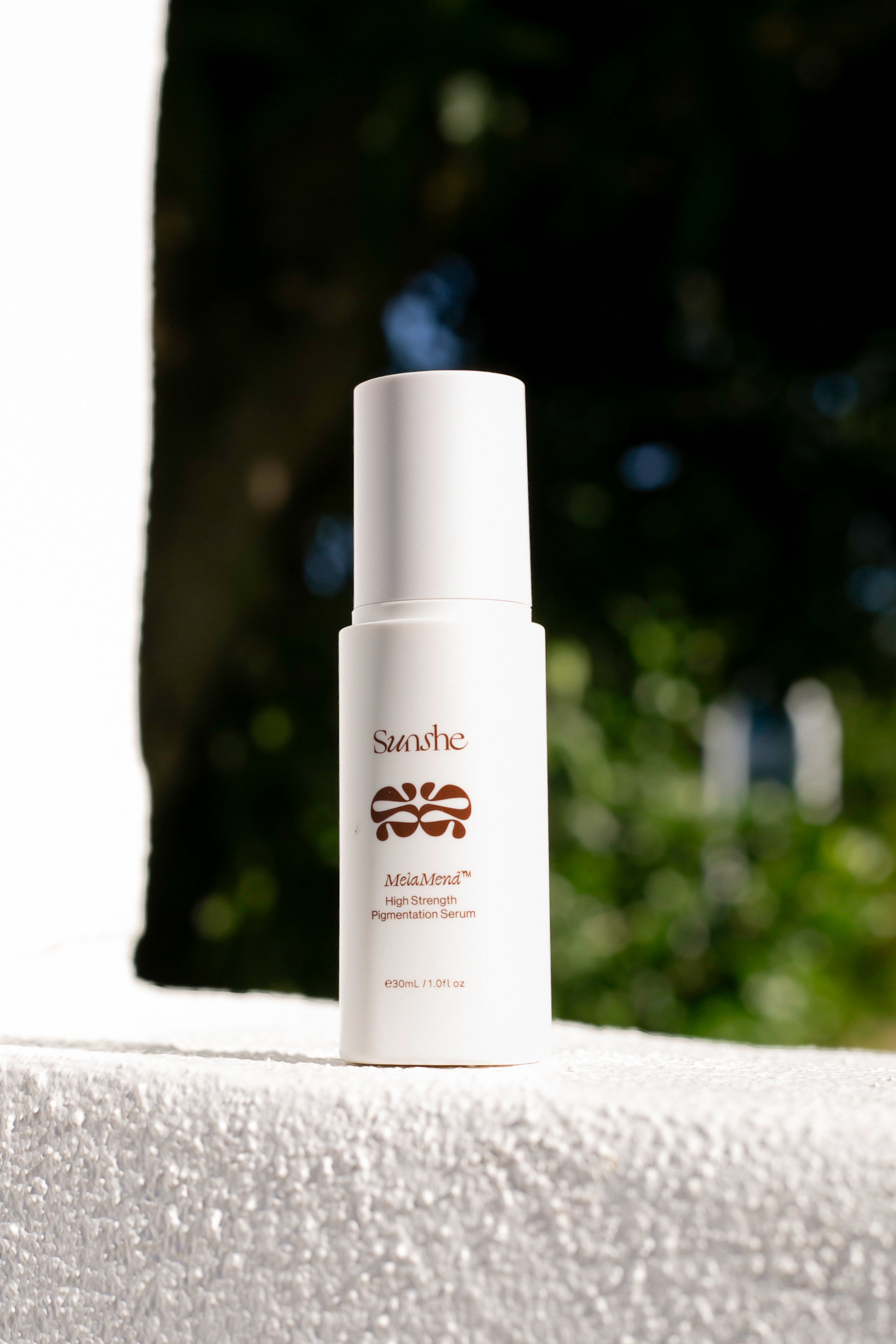 White skincare bottle with brand logo on a light surface with blurred greenery in the background