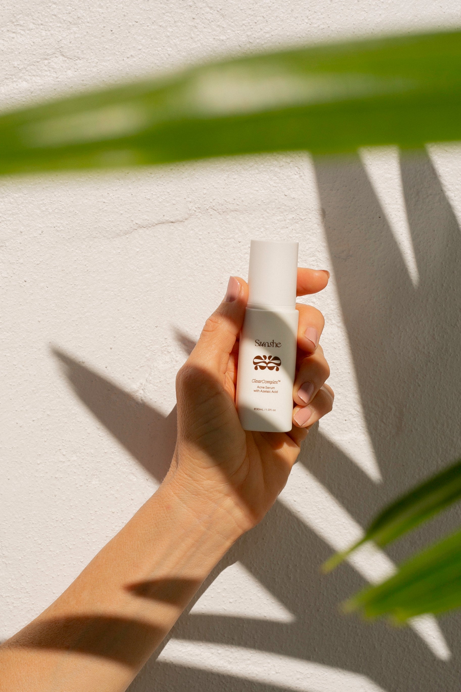 Hand holding a white bottle with 'NATRUE' branding against a light background with leaf shadows