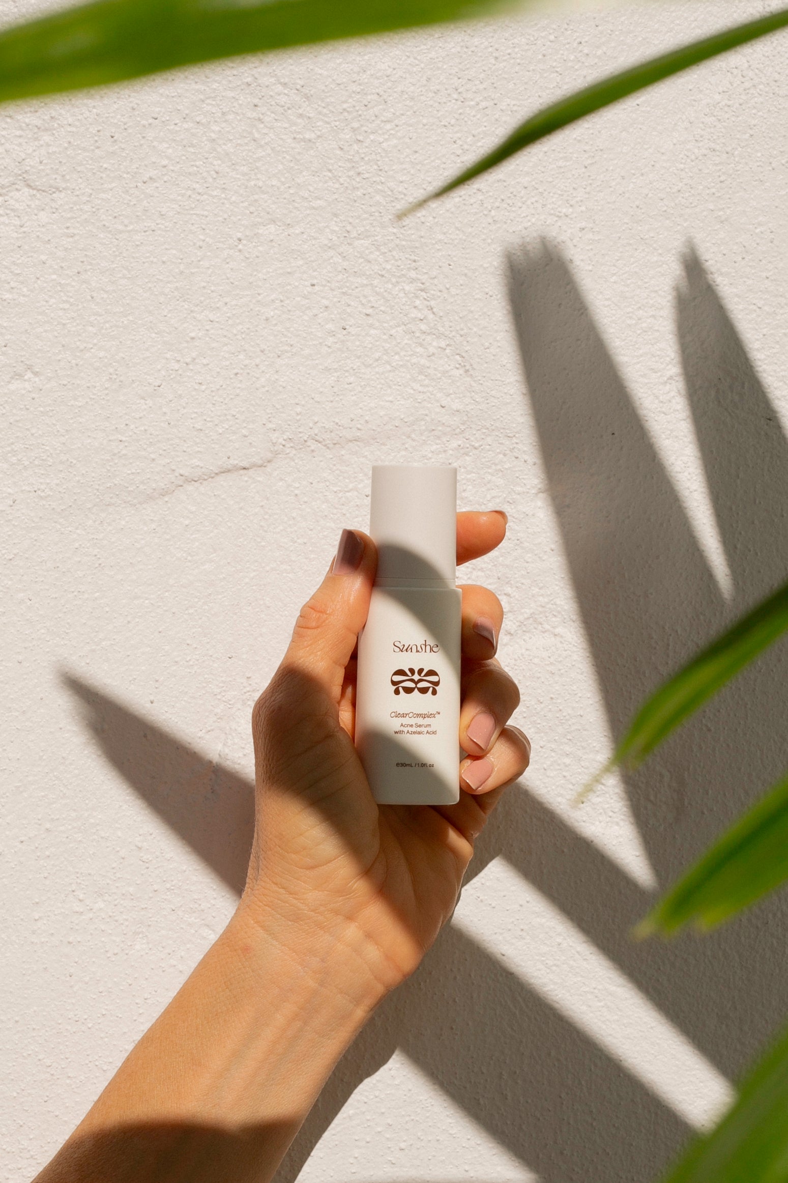 Hand holding a white bottle with a logo against a light background